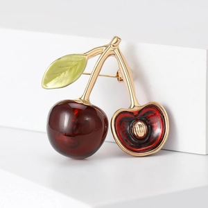 Detailaufnahme einer süßen Kirsch-Emaille-Brosche mit roten Früchten und goldenen Blättern