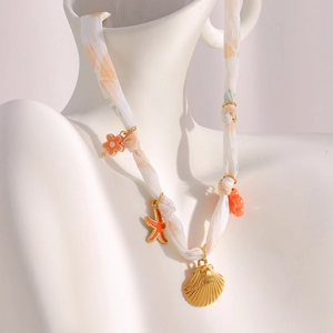 Detail of 18K gold starfish and seashell pendants on orange pattern ribbon necklace