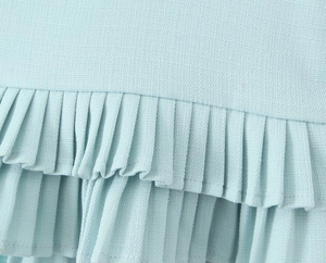 Detail of light blue pleated fabric showing fine knit texture and layered ruffle design