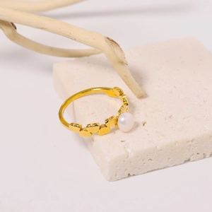 Bague cœur en titane doré avec perle blanche sur un support en pierre minimaliste
