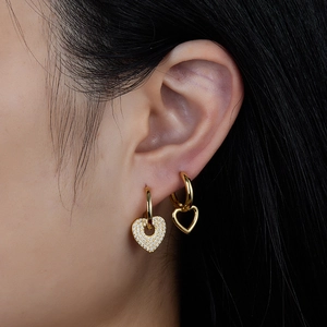 Close-up of gold heart stud and hoop earrings set with zircons worn by a model