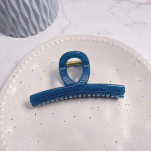 Top view of deep blue glossy hair claw clip with golden spring on ceramic tray