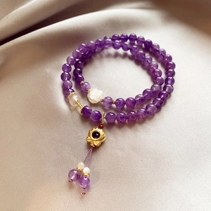 Detailed macro shot of purple amethyst beaded bracelet with gold lotus charm on silk