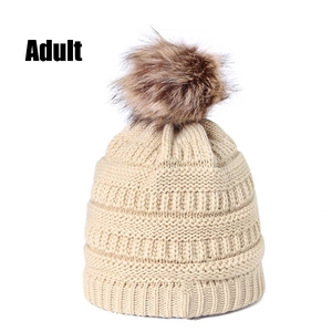 Close-up of beige knit beanie with thick ribbing and large brown faux fur pom-pom