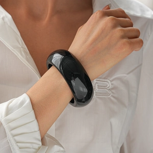 Close-up of minimalist wide black resin bangle with glossy polished finish on model