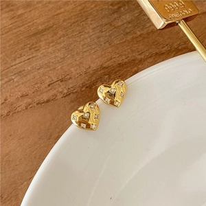 Macro detail of heart-shaped gold studs with inset zircon stones on a white ceramic plate