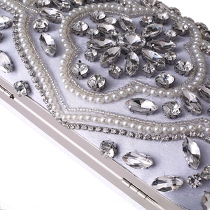 Macro detail of silver satin evening clutch with white pearls and sparkling rhinestones