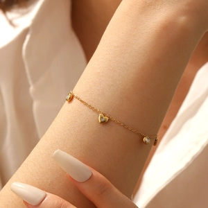 Detailed view of a gold plated bracelet with heart charm and round zircon on a wrist