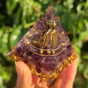 Detailed close-up of handmade Orgone pyramid featuring amethyst, gold foil, and Buddha statue
