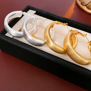 Minimalist matte brushed gold and silver hoop earrings on a black leather jewelry case