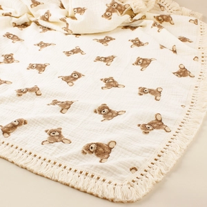 Detail of baby swaddle blanket featuring brown bear prints and delicate tassel edges