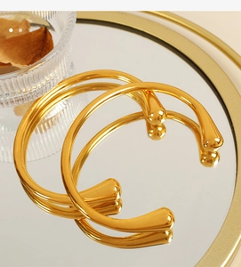 Dettaglio macro del bracciale aperto dorato con punte a goccia lucide su vassoio a specchio