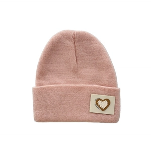 Detail of pink knitted beanie with a heart leather patch and fine ribbed wool texture