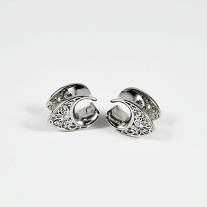 Detailed macro view of silver steel ear plugs with hollow patterns and blue opals