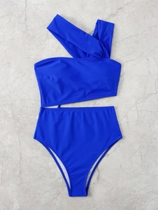 Detailed flat lay of royal blue one-shoulder bikini with high-waisted bottoms on marble