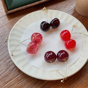 Detailed view of four cherry-shaped earrings in red and pink on a white porcelain plate