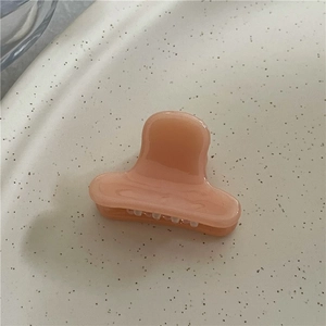 Close-up of peach pink acetate hair claw clip with a glossy resin finish on beige surface