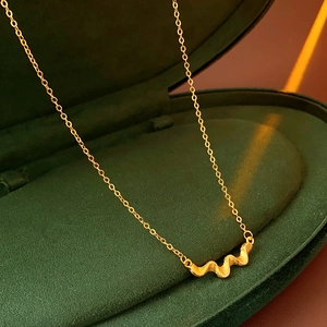 Macro shot of gold-plated wavy pendant necklace displayed in a green velvet jewelry box