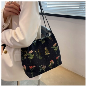 Close-up of black canvas tote bag featuring vibrant floral embroidery and slim shoulder straps