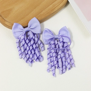 Pair of purple bow hair ties with spiral curly tassels on a rustic wood tray