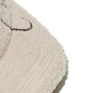 Close-up of beige lamb wool texture with brown embroidered lines on a baseball cap