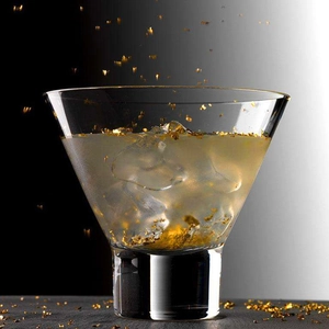 Edible gold foil flakes floating in a cocktail glass with ice and yellow liquid