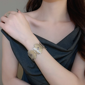 Detail of brushed metal leaf bangle and butterfly ring set on model wrist