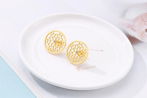 Detailed view of gold circular hollow earrings with tiny zircons on a white ceramic dish