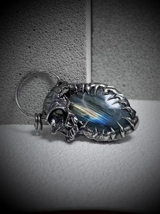 Macro shot of gothic silver skull pendant featuring blue glow labradorite gemstone