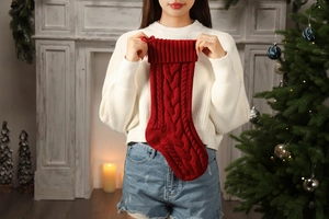 Close-up of red cable knit Christmas stocking held by hands against a festive background