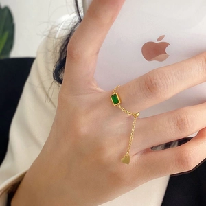 Detail of adjustable gold chain ring featuring a green zircon and heart pendant