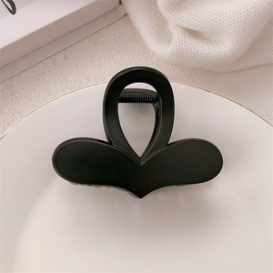 Close-up of a matte black butterfly hair claw clip on a white plate with soft lighting