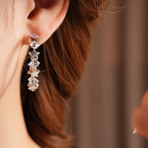 Close-up of sparkling star-shaped silver earrings with zircon inlay worn by a model