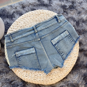 Dettaglio di pantaloncini di denim a vita alta con orlo sfrangiato e tasche con patta