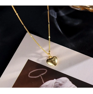 Close-up of a luxury gold heart pendant necklace displayed on a beige card backdrop