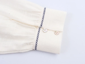 Detail of cream cotton linen sleeve featuring blue cross-embroidery and pearly buttons
