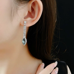 Detailed view of silver tassel earrings with green gems worn by a model against black