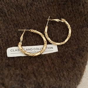 Detailed close-up of matte gold twisted rope hoop earrings on brown knit fabric