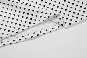 Macro detail of white polka dot dress fabric showing fine stitching and sewing quality