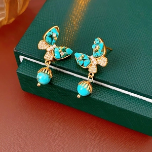 Vue macro de boucles d'oreilles papillon plaquées or avec turquoises sur un écrin à bijoux
