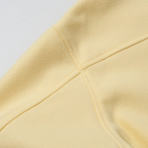 Macro view of creamy yellow wool fabric texture and fine stitching on the short coat
