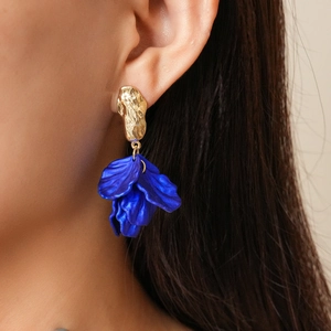Detail of bohemian gold hook earrings with blue acrylic flower petals on a model
