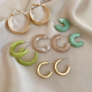 Detailed close-up of acrylic resin and gold hoop earrings on luxury champagne silk fabric