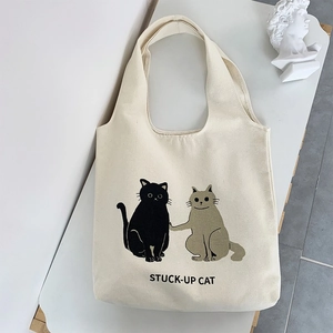 Top view of cream canvas tote bag featuring cute cartoon cats and Stuck-Up Cat text