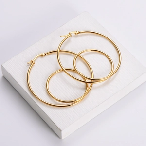 Polished gold stainless steel hoop earrings in two sizes on a white textured stand