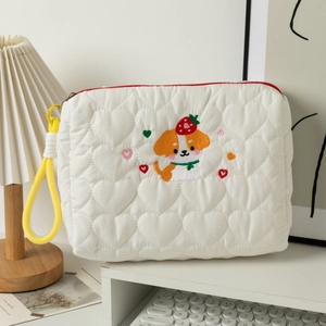 Quilted white cosmetic bag with cute puppy embroidery and yellow handle on a desk