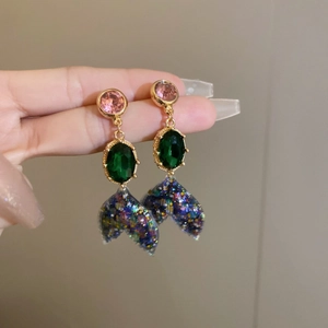 Detail of mermaid tail earrings with emerald stones and pink zircons in gold setting