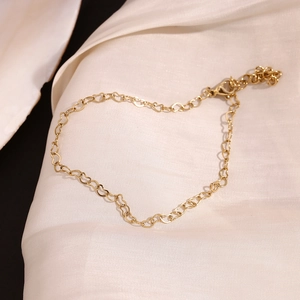 Detail of 14K gold plated heart link anklet with lobster clasp on white silk fabric
