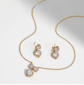 Detailed macro of gold bow and heart zircon necklace and earring jewelry set on white background