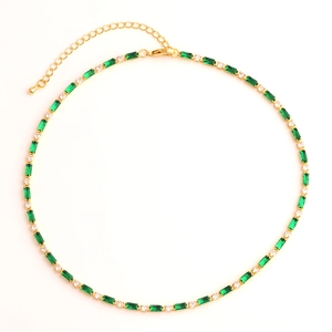 Detail of gold necklace with green rectangular stones and clear round gems on white